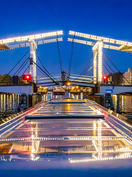 Boat approaching illuminated Skinny Bridge in Amsterdam at night.