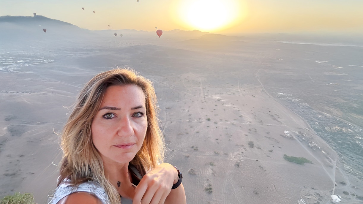 Woman taking selfie in hot air balloon over Marrakech desert at sunrise.