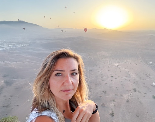 Woman taking selfie in hot air balloon over Marrakech desert at sunrise.