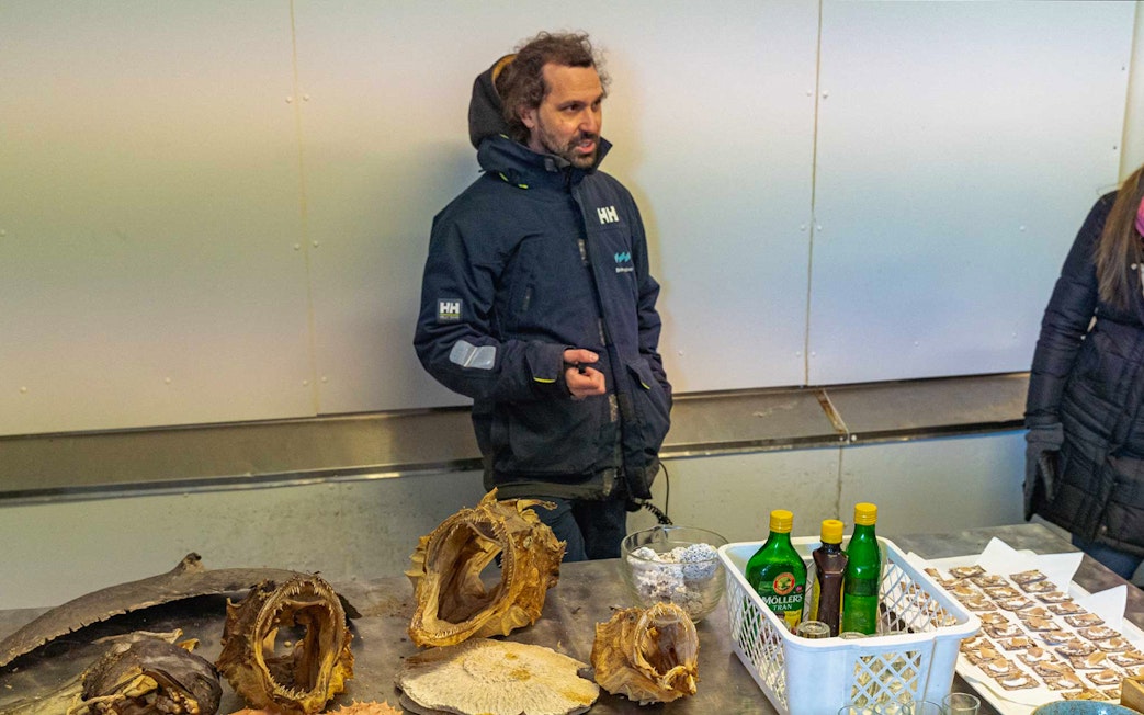 Man presenting dried fish heads and bottles on a table in a seafood market.