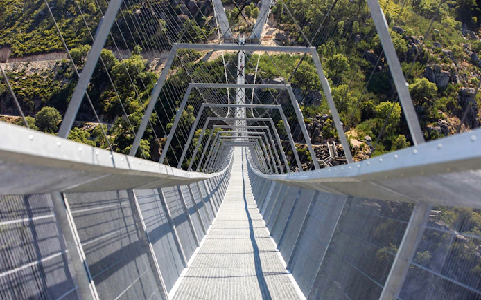 Pedestrian view of 516 Arouca suspension bridge spanning a lush valley in Portugal.