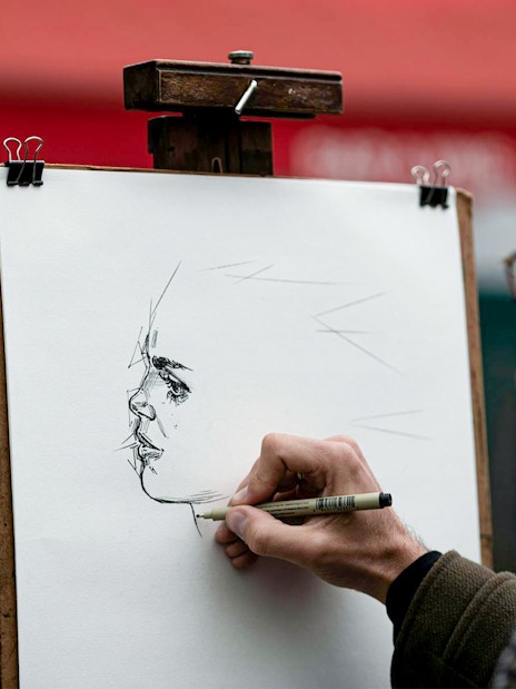 Artist sketching a portrait on a street in Montmartre during an English guided tour.