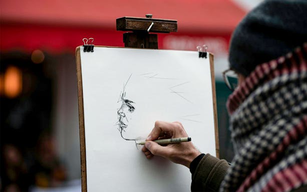 Artist sketching a portrait on a street in Montmartre during an English guided tour.