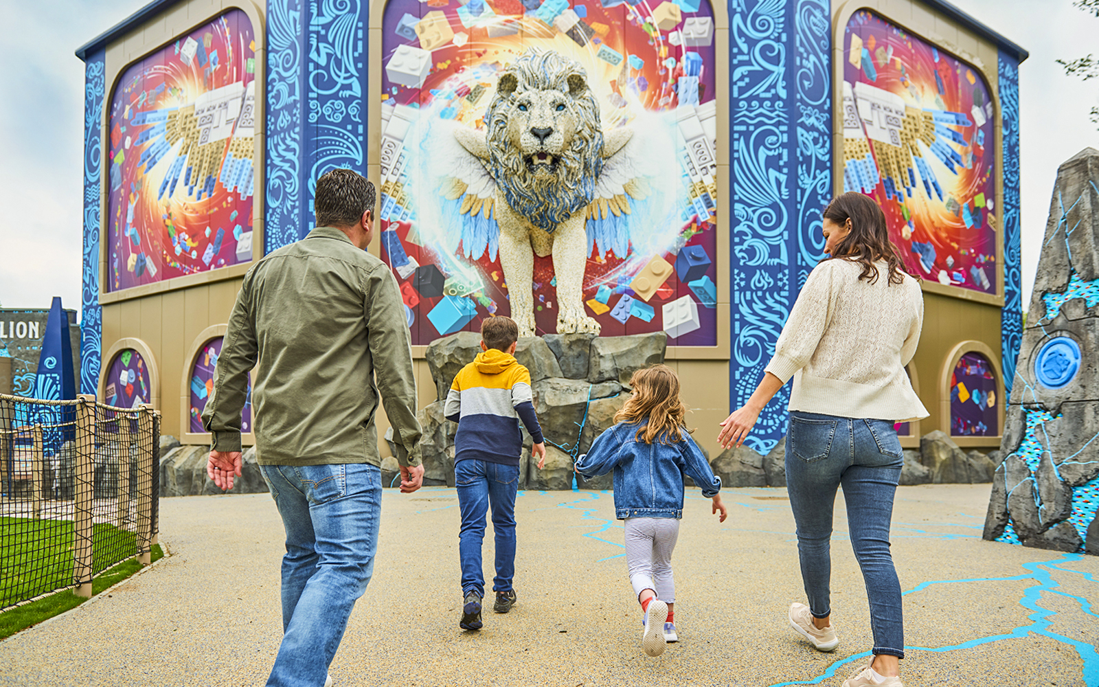 Family approaching a colorful LEGO lion mural at a theme park.