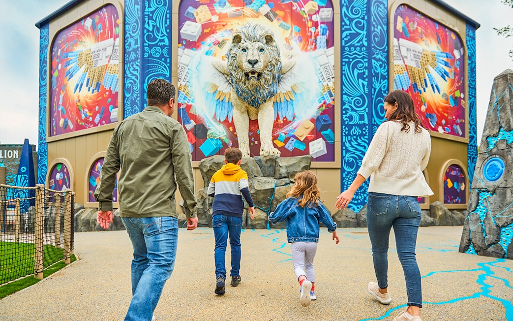 Family approaching a colorful LEGO lion mural at a theme park.