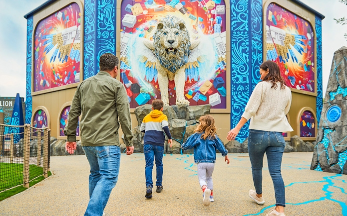 Family approaching a colorful LEGO lion mural at a theme park.