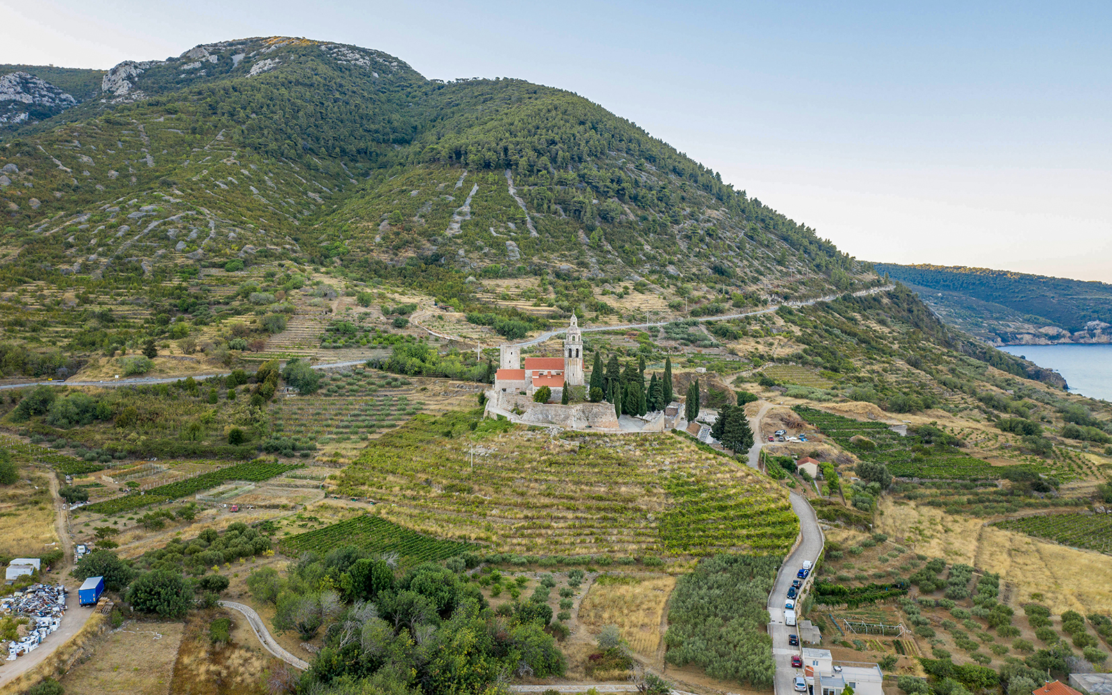 Aerial view of St. Nicolas Church on Mount Hum in Komiza, surrounded by terraced fields and hills.