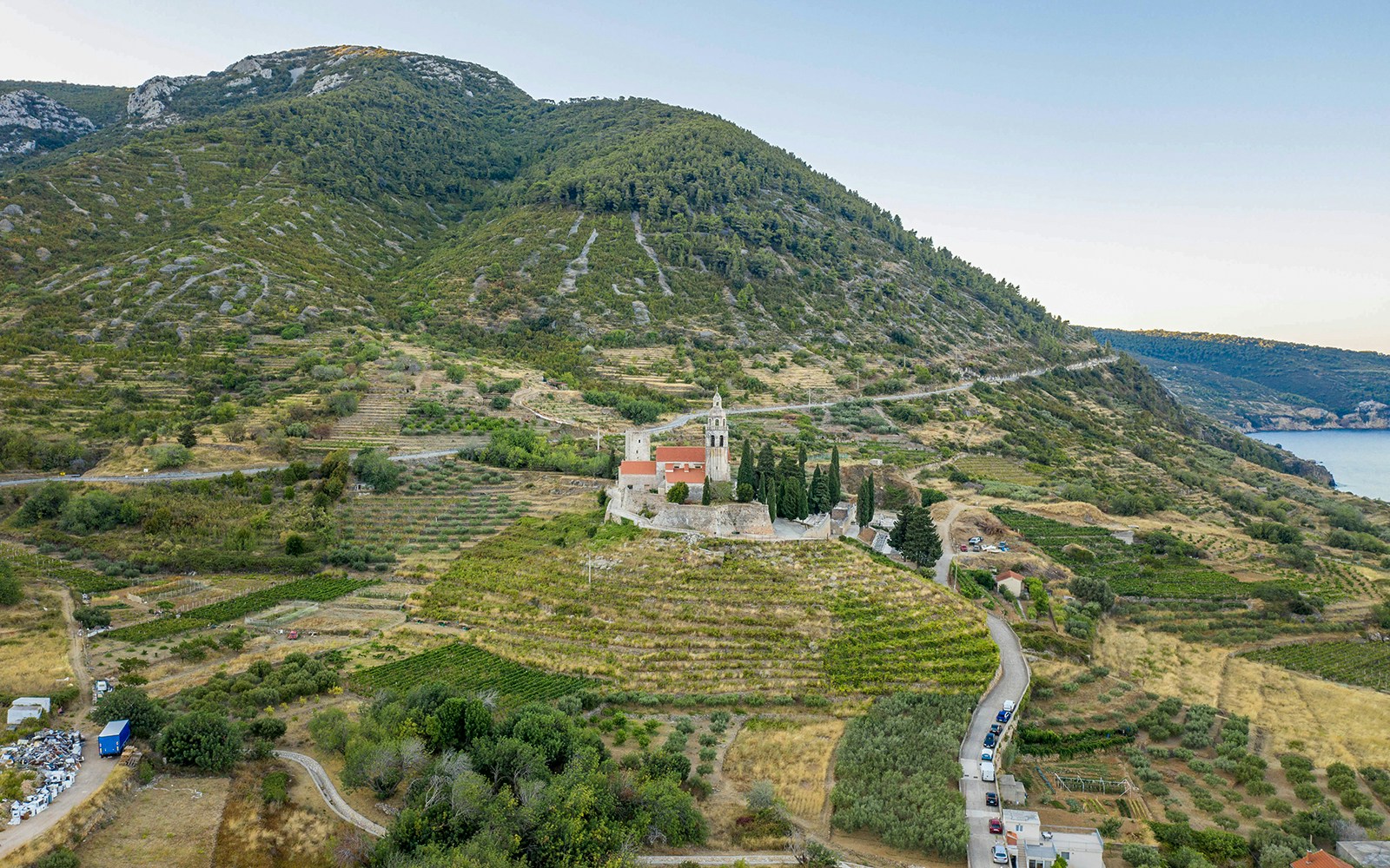 Aerial view of St. Nicolas Church on Mount Hum in Komiza, surrounded by terraced fields and hills.