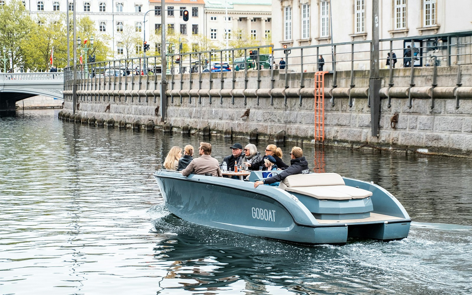 Guests on electric boat tour in Copenhagen, captain pedaling through city canals.