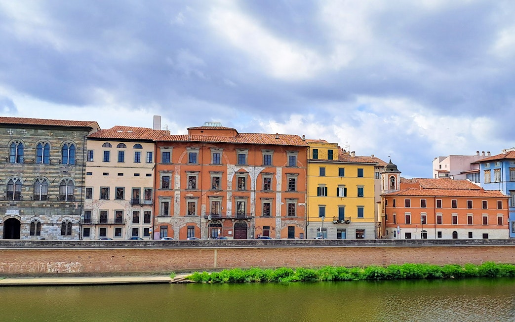 Colorful historic buildings along the Arno River in Pisa, Italy.