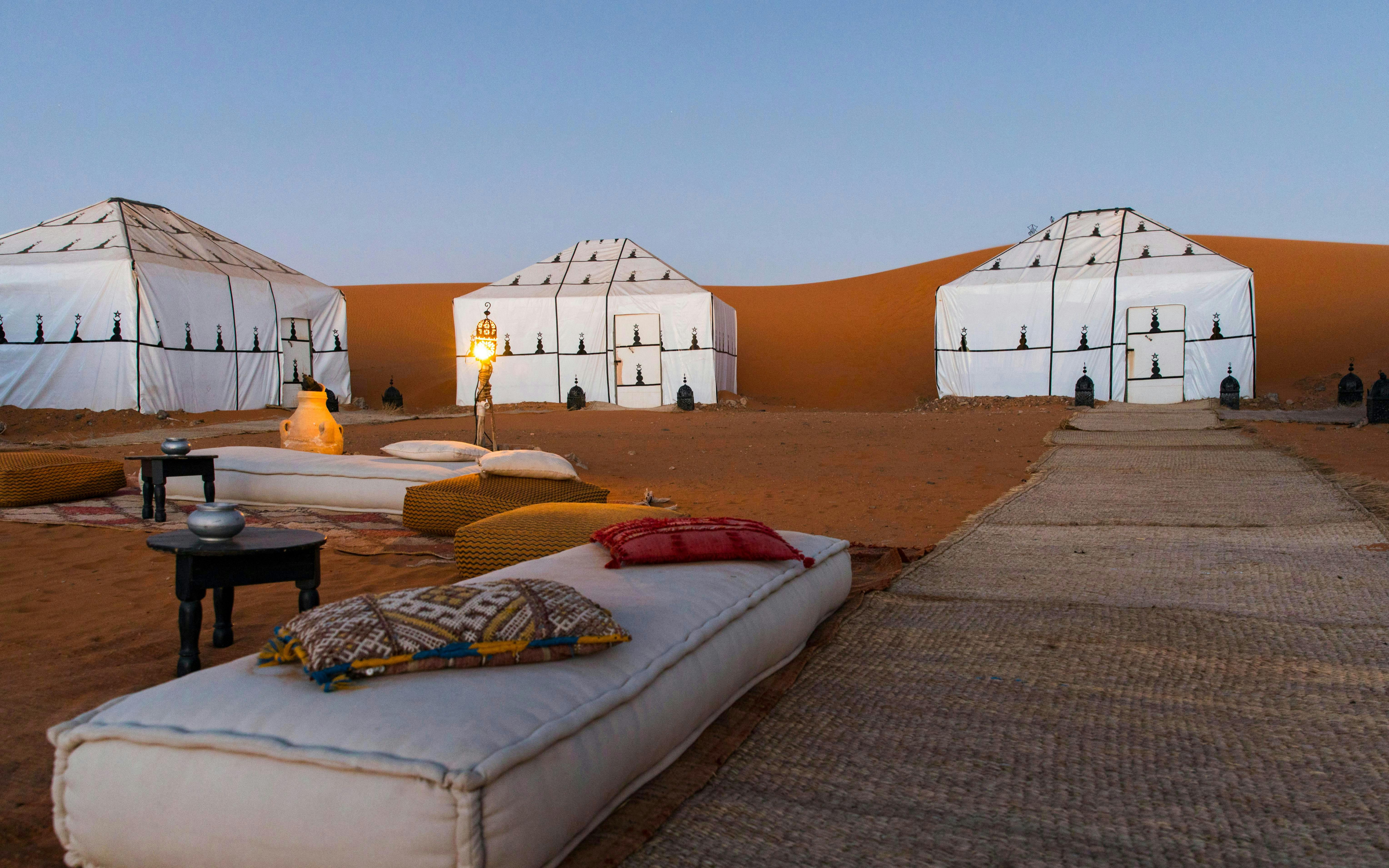 Luxury desert camp with white tents and lanterns in Sahara.