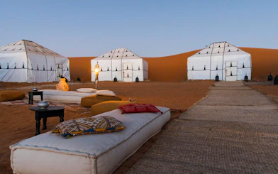 Luxury desert camp with white tents and lanterns in Sahara.