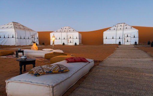 Luxury desert camp with white tents and lanterns in Sahara.