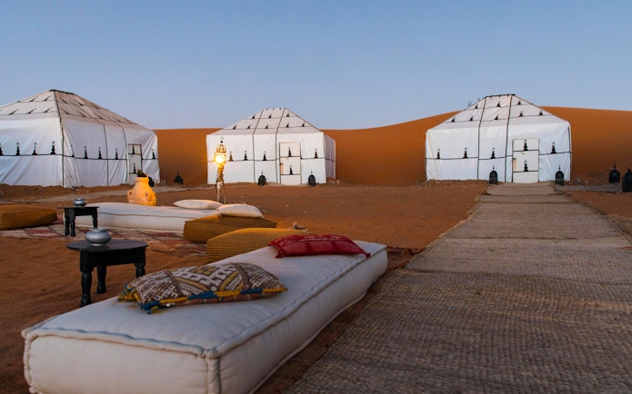 Luxury desert camp with white tents and lanterns in Sahara.