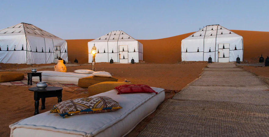 Luxury desert camp with white tents and lanterns in Sahara.
