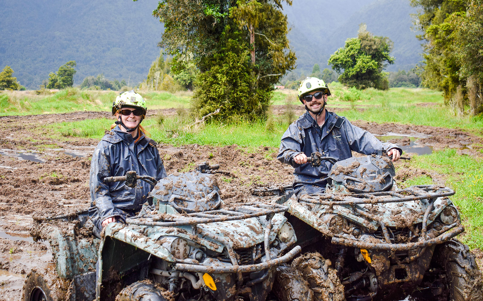 Quad biking through muddy trails at Franz Josef, New Zealand with lush forest backdrop.