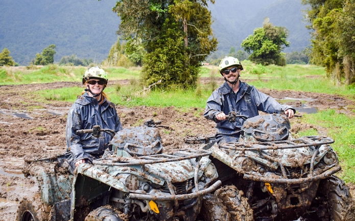 Quad biking through muddy trails at Franz Josef, New Zealand with lush forest backdrop.