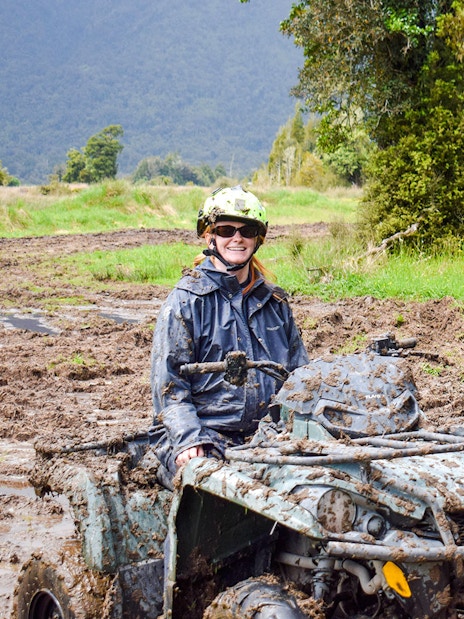 Quad biking through muddy trails at Franz Josef, New Zealand with lush forest backdrop.