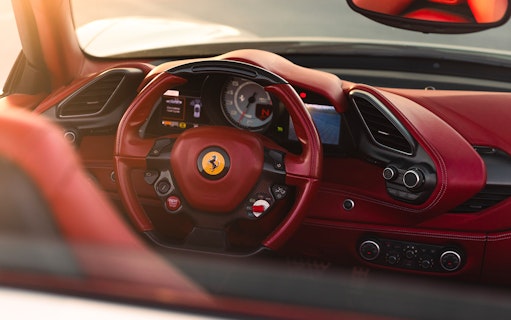 Ferrari interior with red leather steering wheel and dashboard controls.