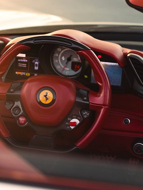 Ferrari interior with red leather steering wheel and dashboard controls.