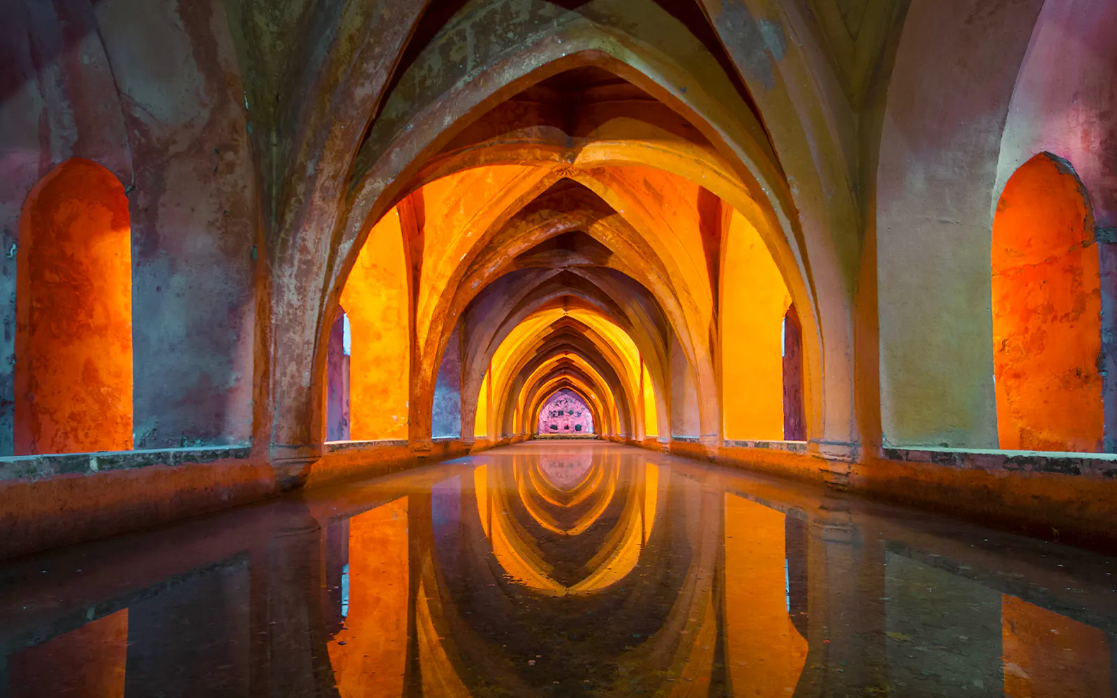 Royal Alcázar of Seville underground tunnel with intricate arches and reflections.