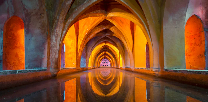 Royal Alcázar of Seville underground tunnel with intricate arches and reflections.