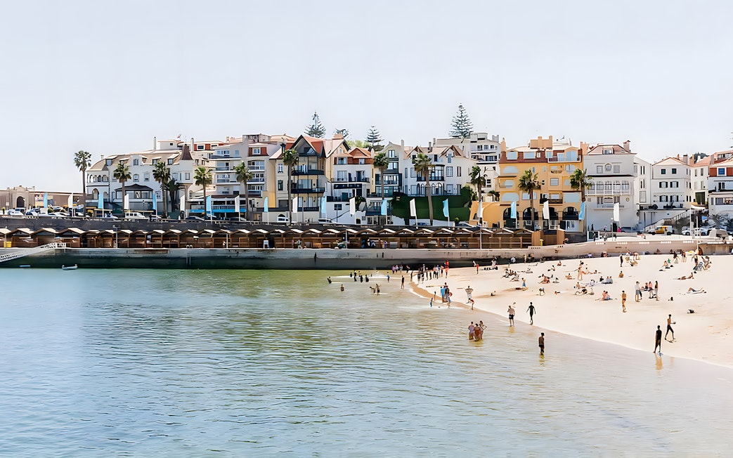 Beachfront in Cascais with people enjoying the sand and water, colorful buildings in the background.