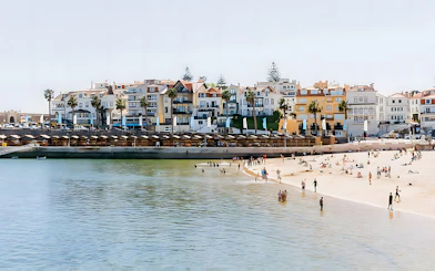 Beachfront in Cascais with people enjoying the sand and water, colorful buildings in the background.