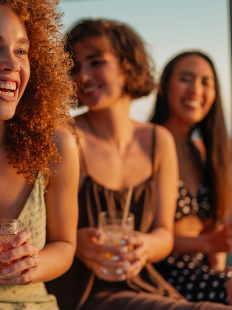 Friends laughing and holding cocktails at sunset during a boat party.