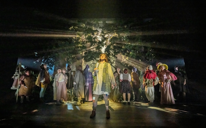 Cast performing in "Into The Woods" with forest backdrop and dramatic lighting.