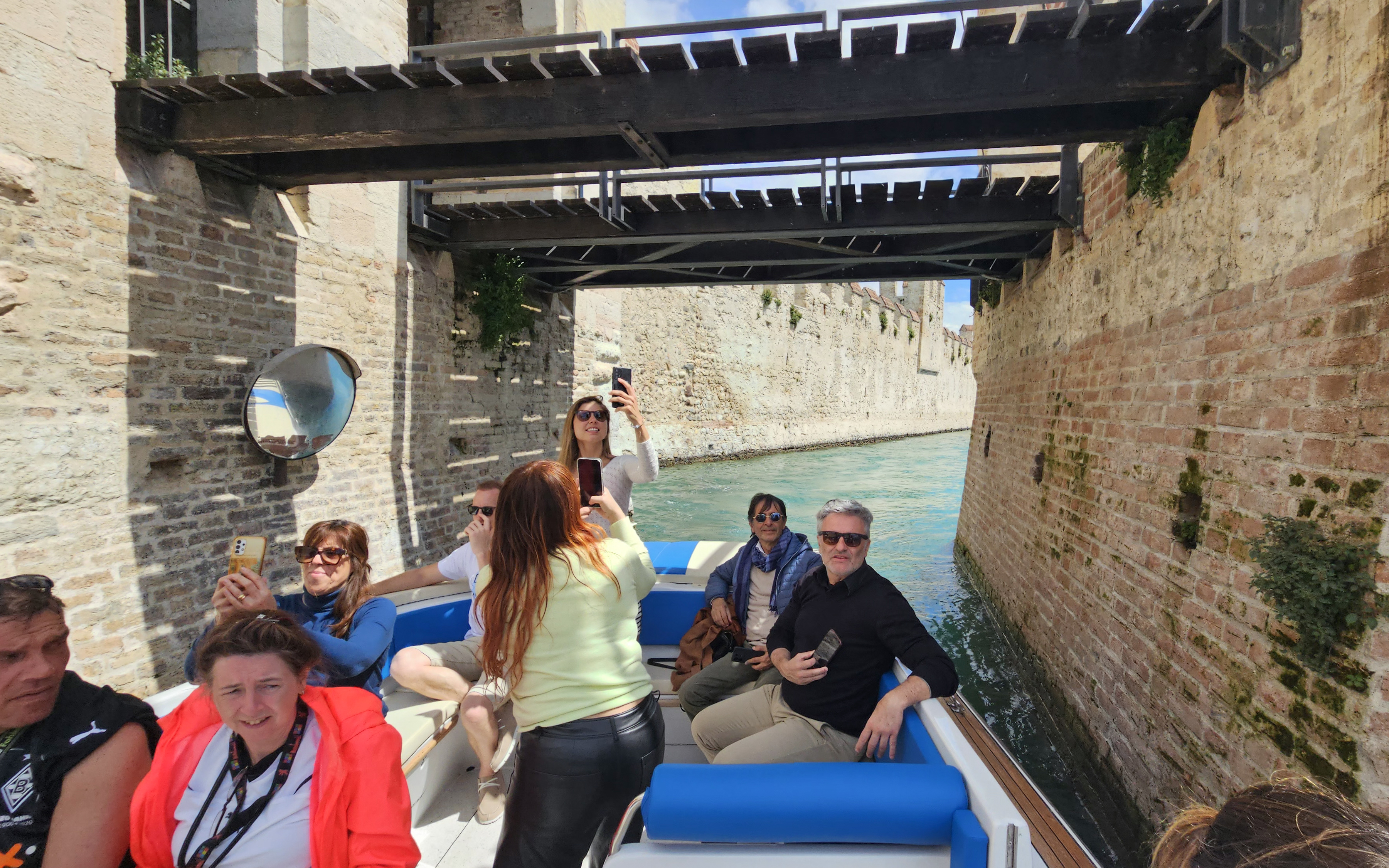 Private boat tour with people taking photos under a bridge in Sirmione, Italy.