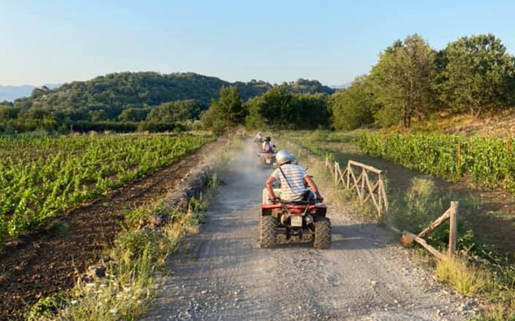 Quad bikes on a dirt path through Alcantara Gorges, Sicily, with lush greenery.