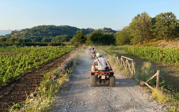 Quad bikes on a dirt path through Alcantara Gorges, Sicily, with lush greenery.