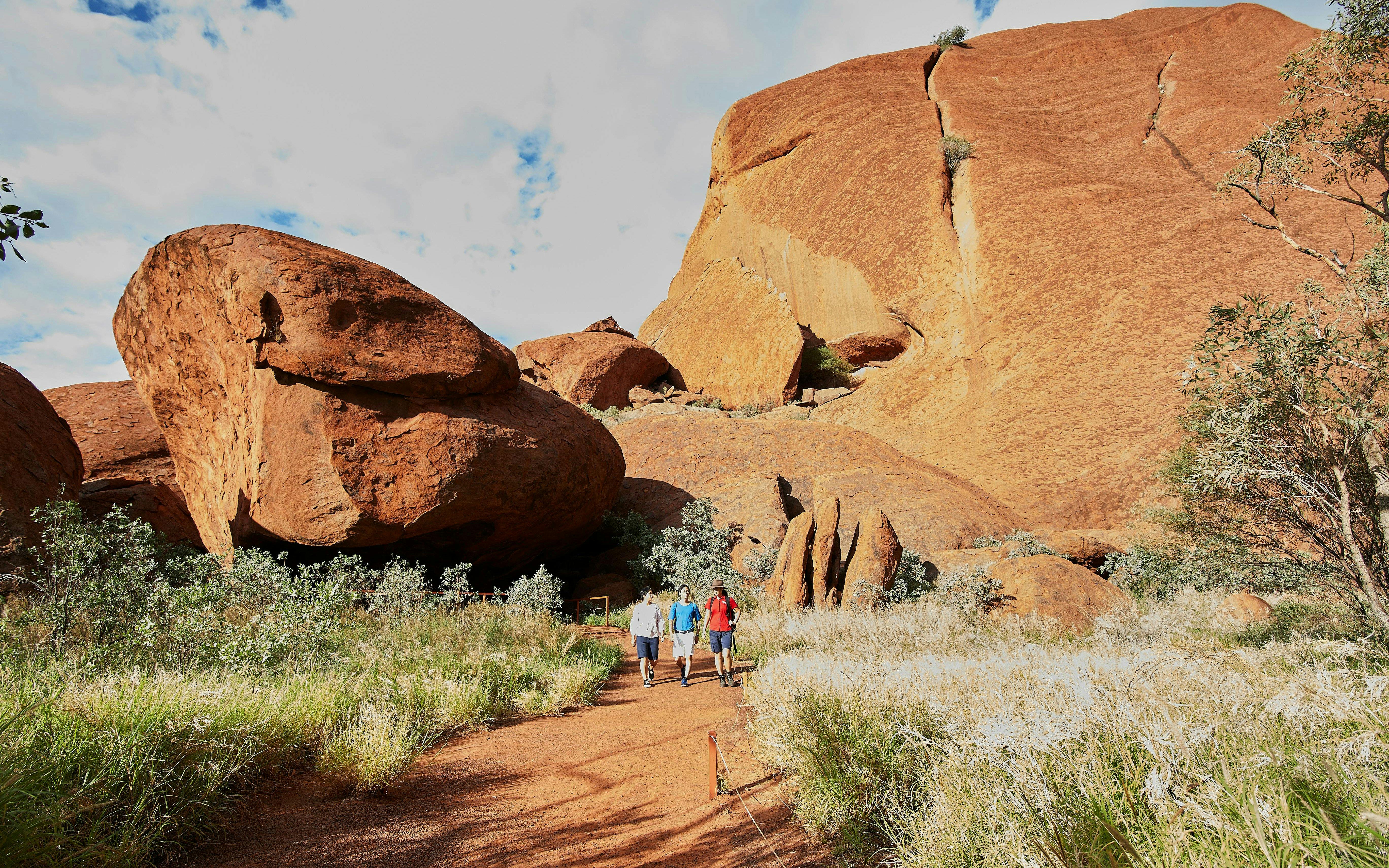Walking tour group at Uluru base, surrounded by red rock formations and greenery, Australia.