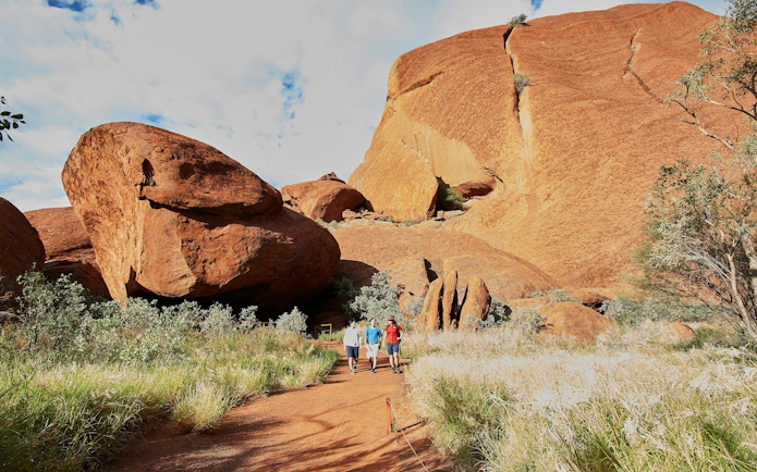 Walking tour group at Uluru base, surrounded by red rock formations and greenery, Australia.