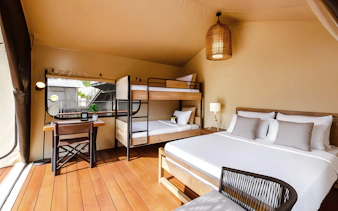 Interior of a tent at Colugo Camp, Mandai Wildlife Reserve, featuring a bed, bunk beds, and a desk.