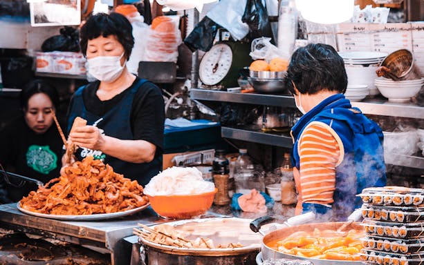 Seoul street food vendors preparing dishes on a walking tour with free samples.