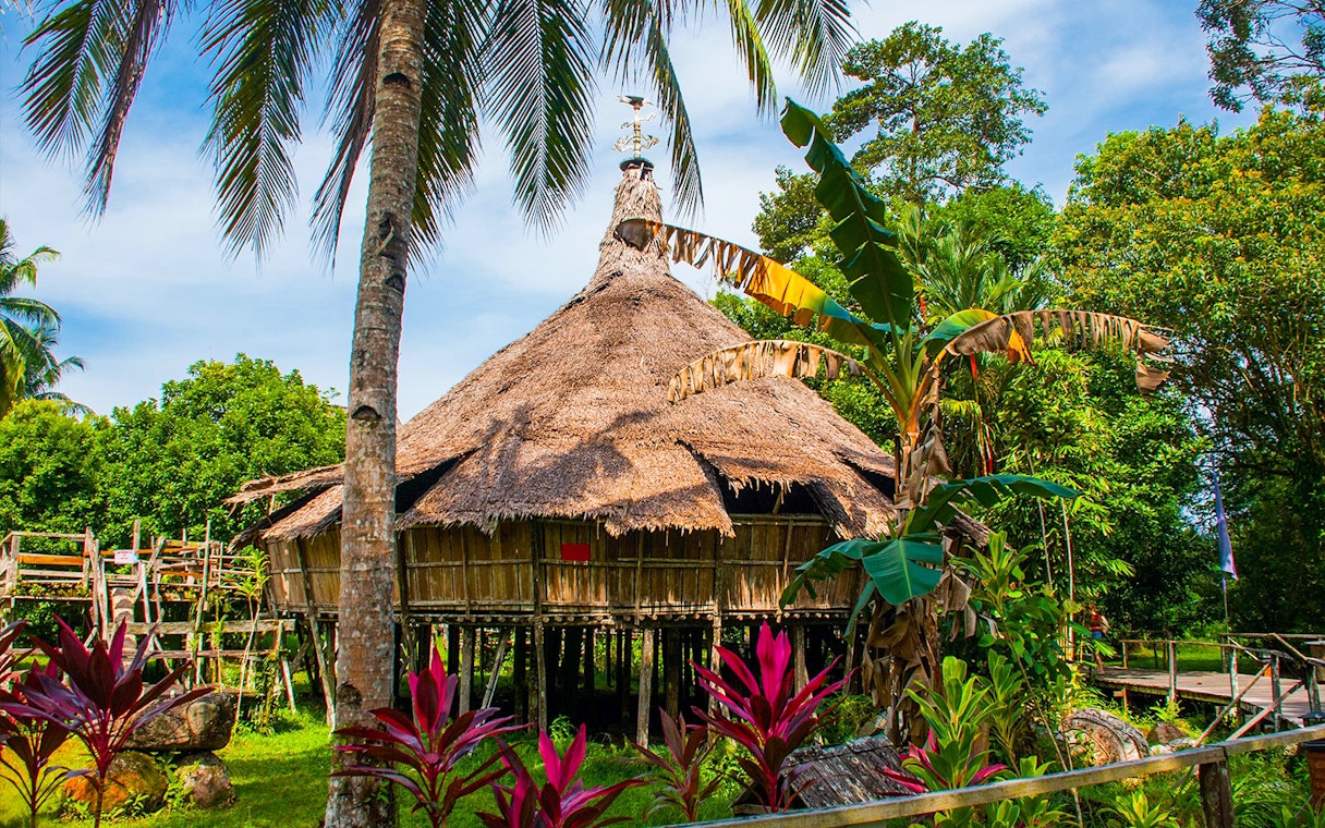 Traditional Borneo longhouse at Sarawak Cultural Village surrounded by lush greenery.