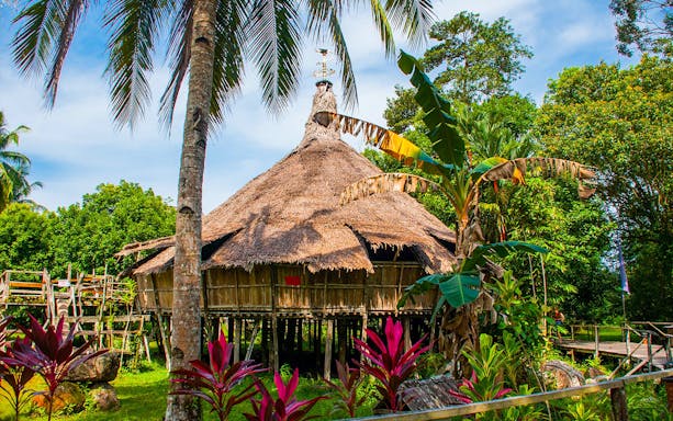 Traditional Borneo longhouse at Sarawak Cultural Village surrounded by lush greenery.