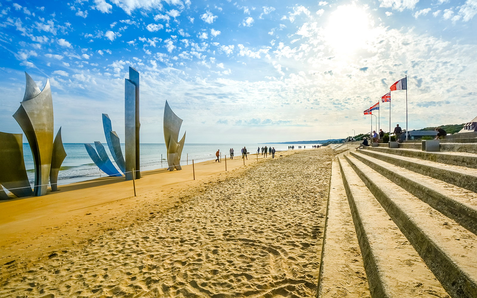 Tourists sit under flags on steps at Omaha Beach near Les Braves Memorial, Normandy.
