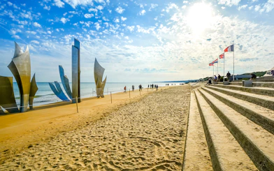Tourists sit under flags on steps at Omaha Beach near Les Braves Memorial, Normandy.