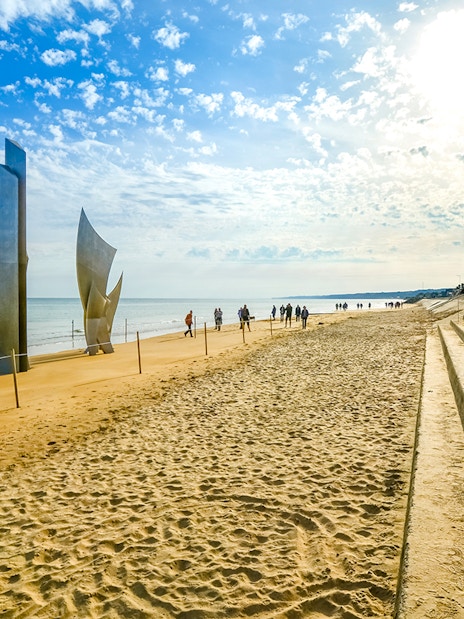 Tourists sit under flags on steps at Omaha Beach near Les Braves Memorial, Normandy.