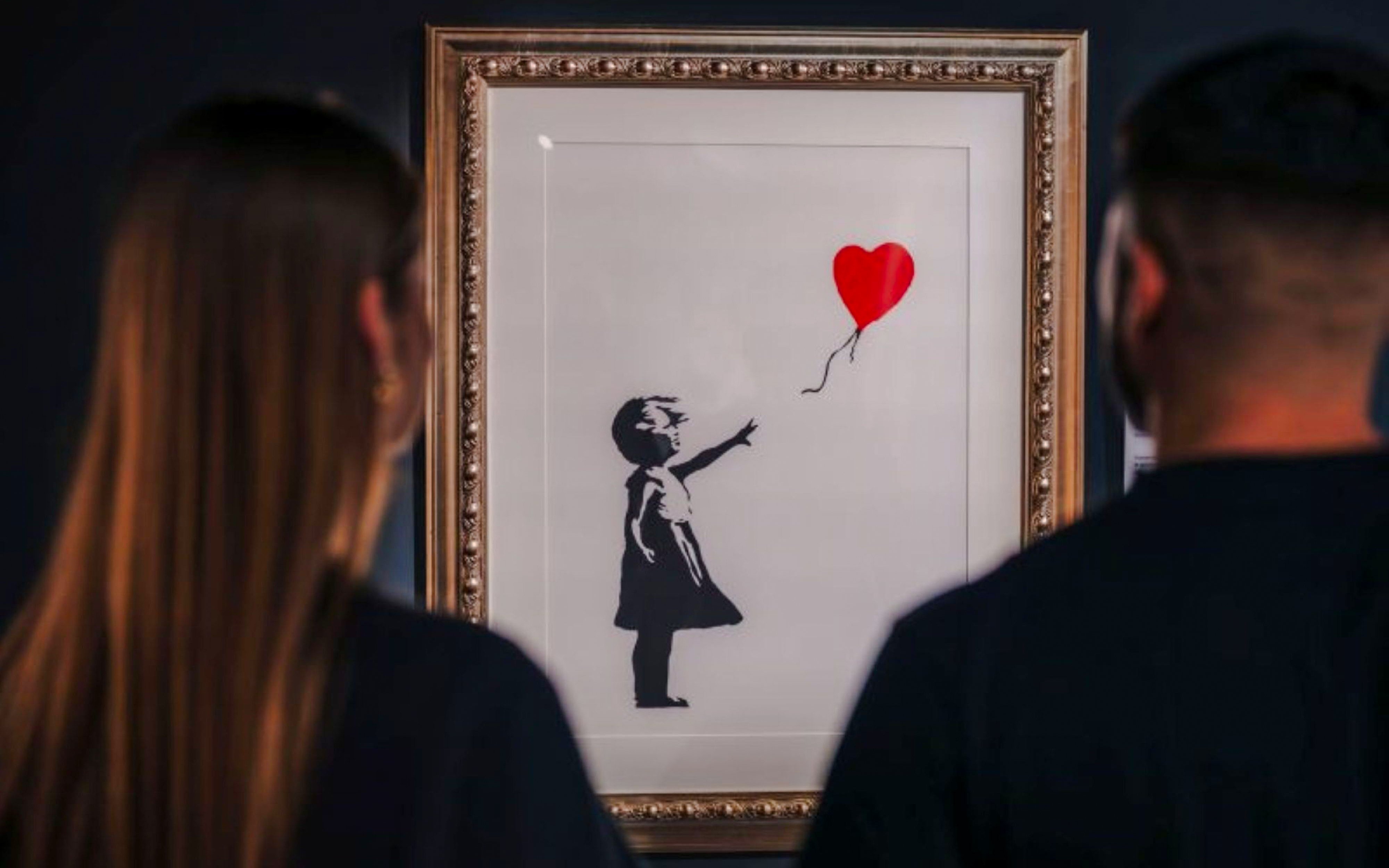 Visitors viewing Banksy's "Girl with Balloon" artwork in a gallery.