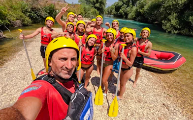 Group ready for Bistrice River rafting adventure near Saranda, holding paddles by the riverbank.