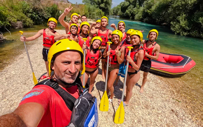 Group ready for Bistrice River rafting adventure near Saranda, holding paddles by the riverbank.