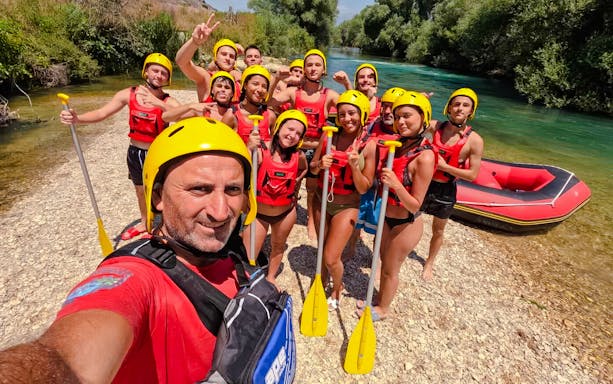 Group ready for Bistrice River rafting adventure near Saranda, holding paddles by the riverbank.
