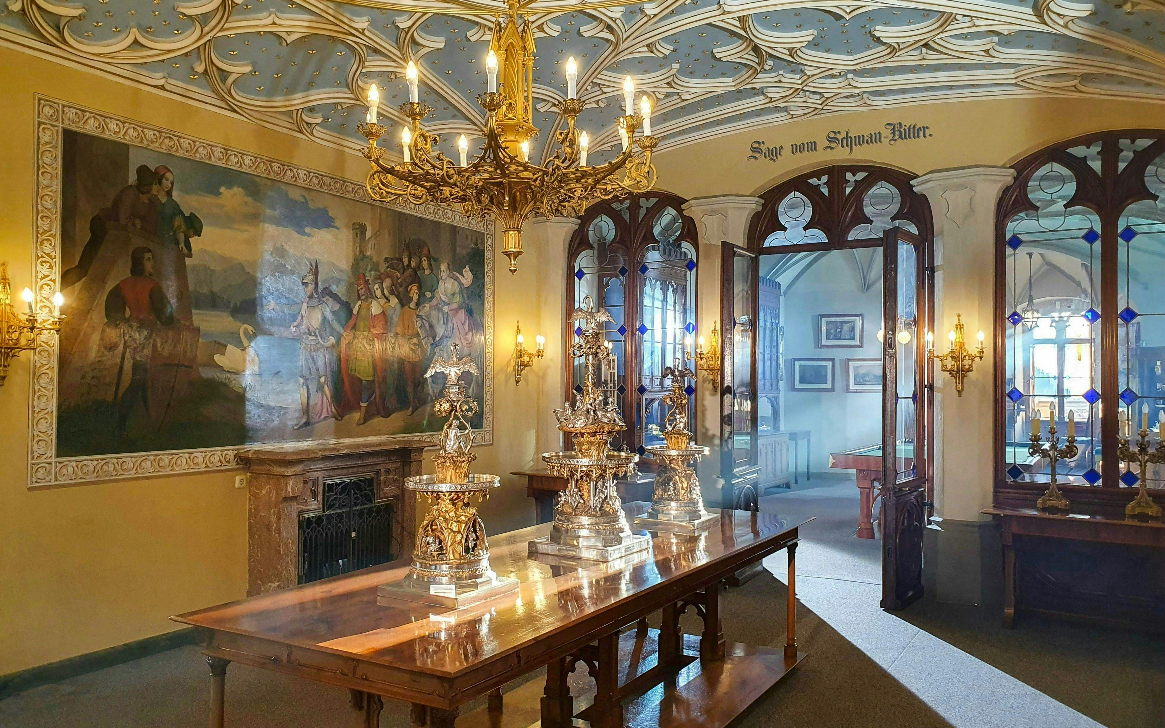 Hohenschwangau Castle interior with ornate chandelier, mural, and decorative silverware in Bavaria.