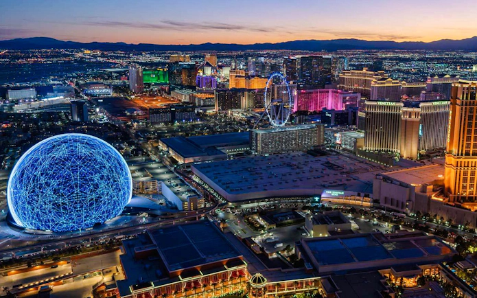 Las Vegas skyline at dusk with illuminated Sphere and Ferris wheel, view from helicopter tour.
