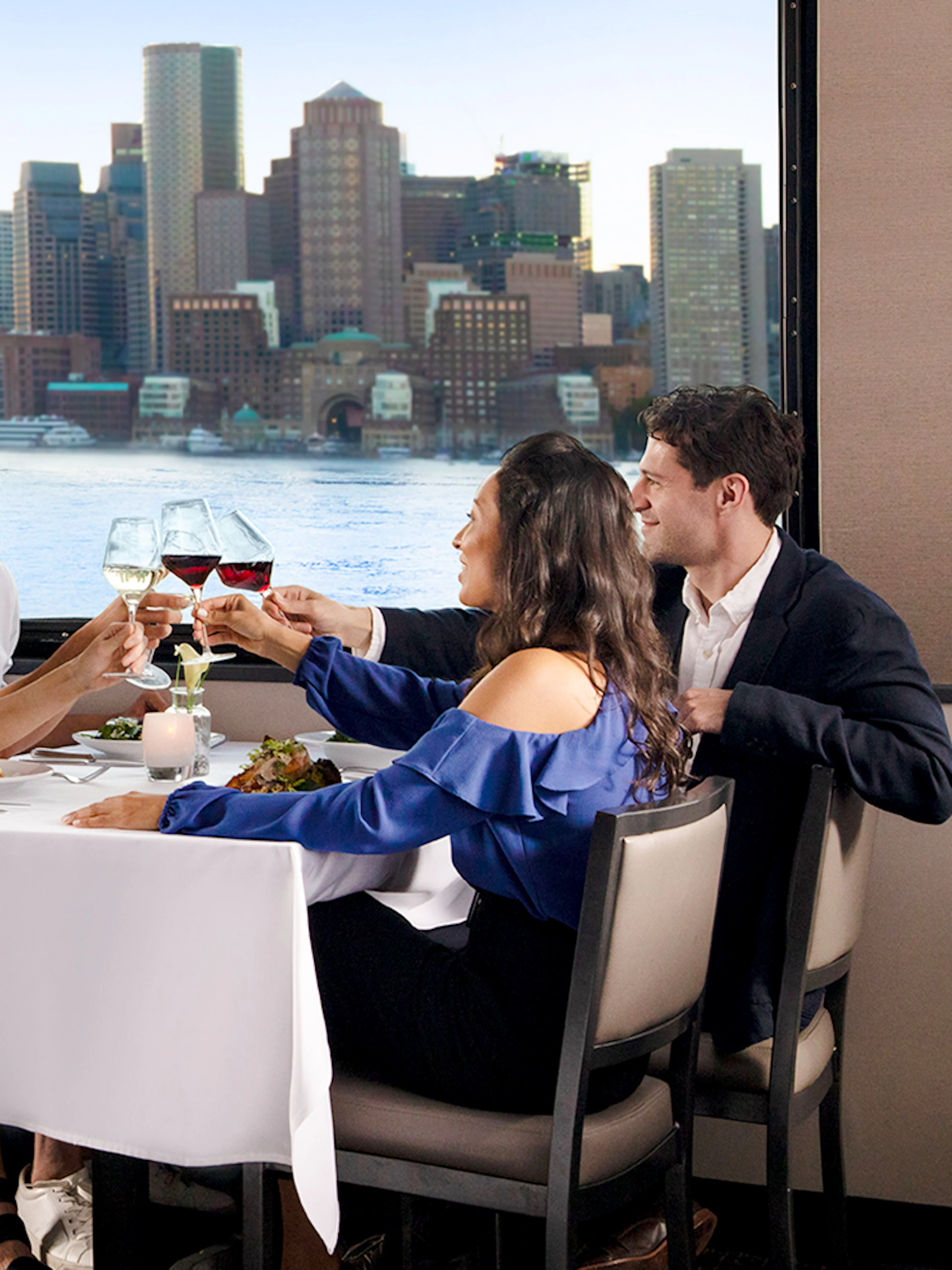 Dining guests enjoying a meal with Boston skyline view on Premier Dinner Cruise on Odyssey.