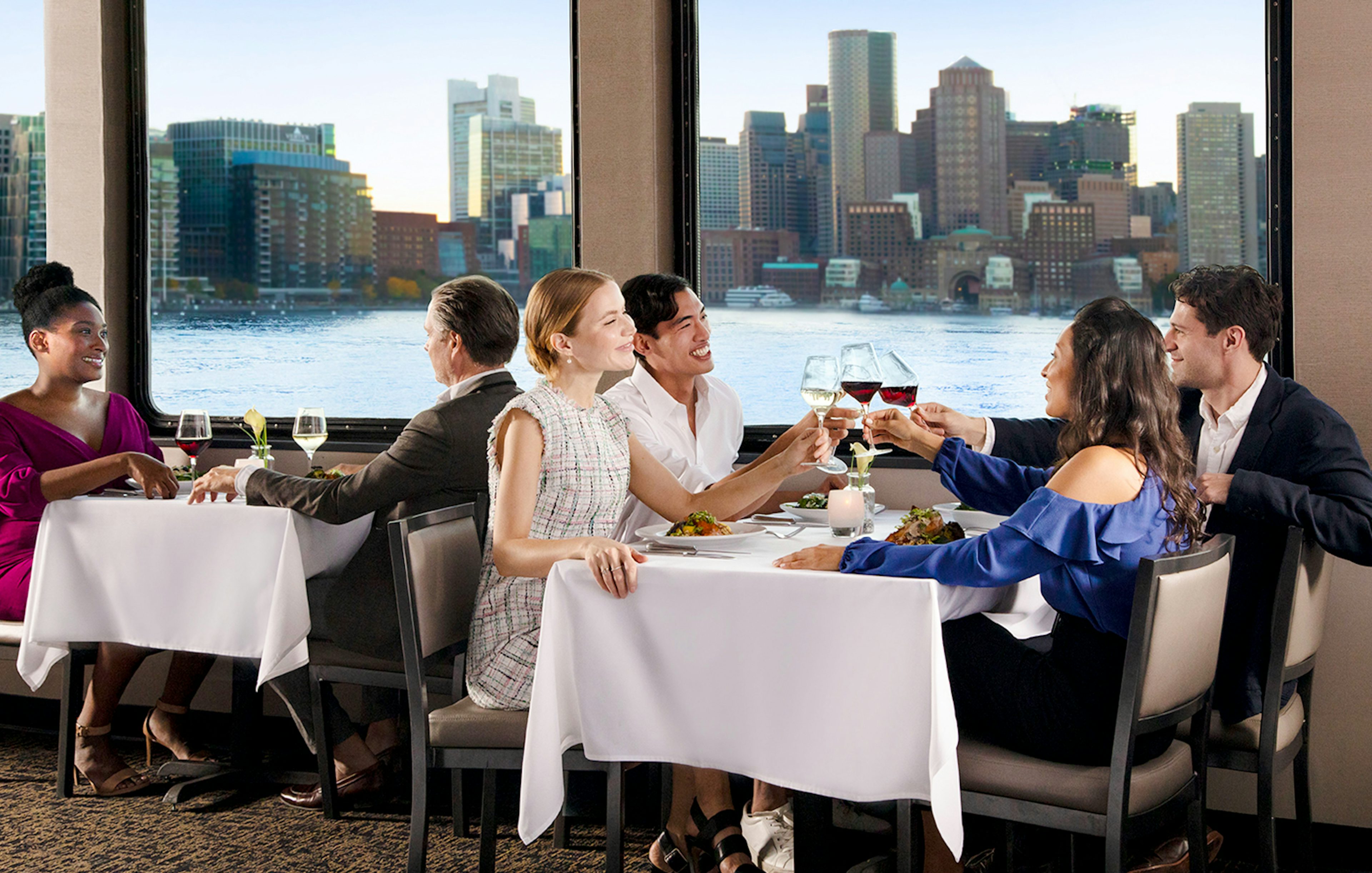 Dining guests enjoying a meal with Boston skyline view on Premier Dinner Cruise on Odyssey.